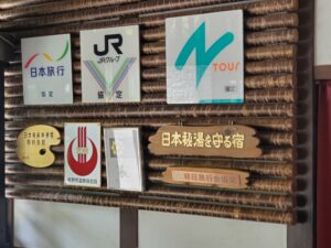 日本秘湯を守る宿の木製看板と提携旅行会社のロゴ